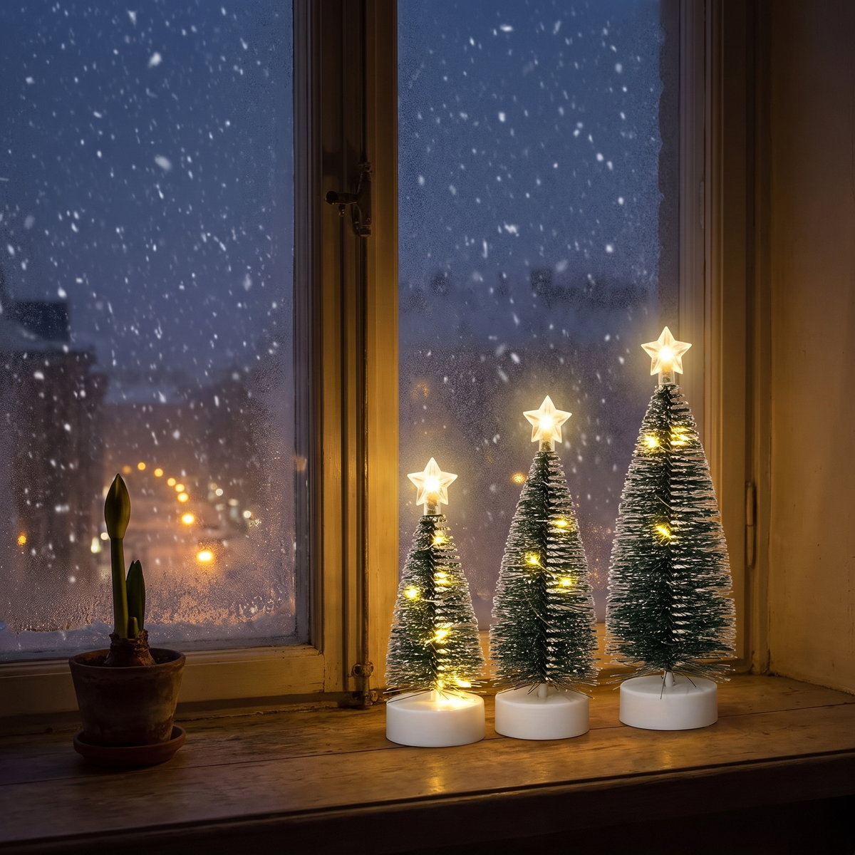 Silva: tre små julgranar med varmvitt ljus på fönsterbrädan en snöig decemberkväll