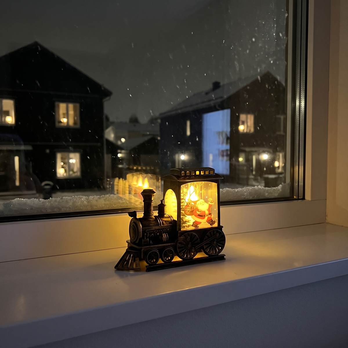 Julius tänd på fönsterbrädan en snöig kväll, grannhusen lyser utanför
