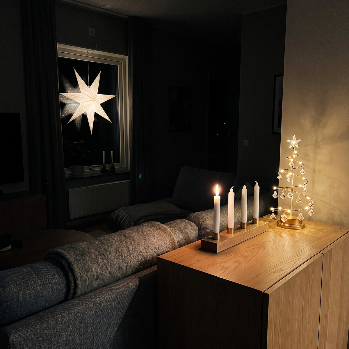 Ett mörkt vardagsrum i början av december: Tindra lyser på skänken, ett ljus tänt i adventsljusstaken och stjärnan i fönstret