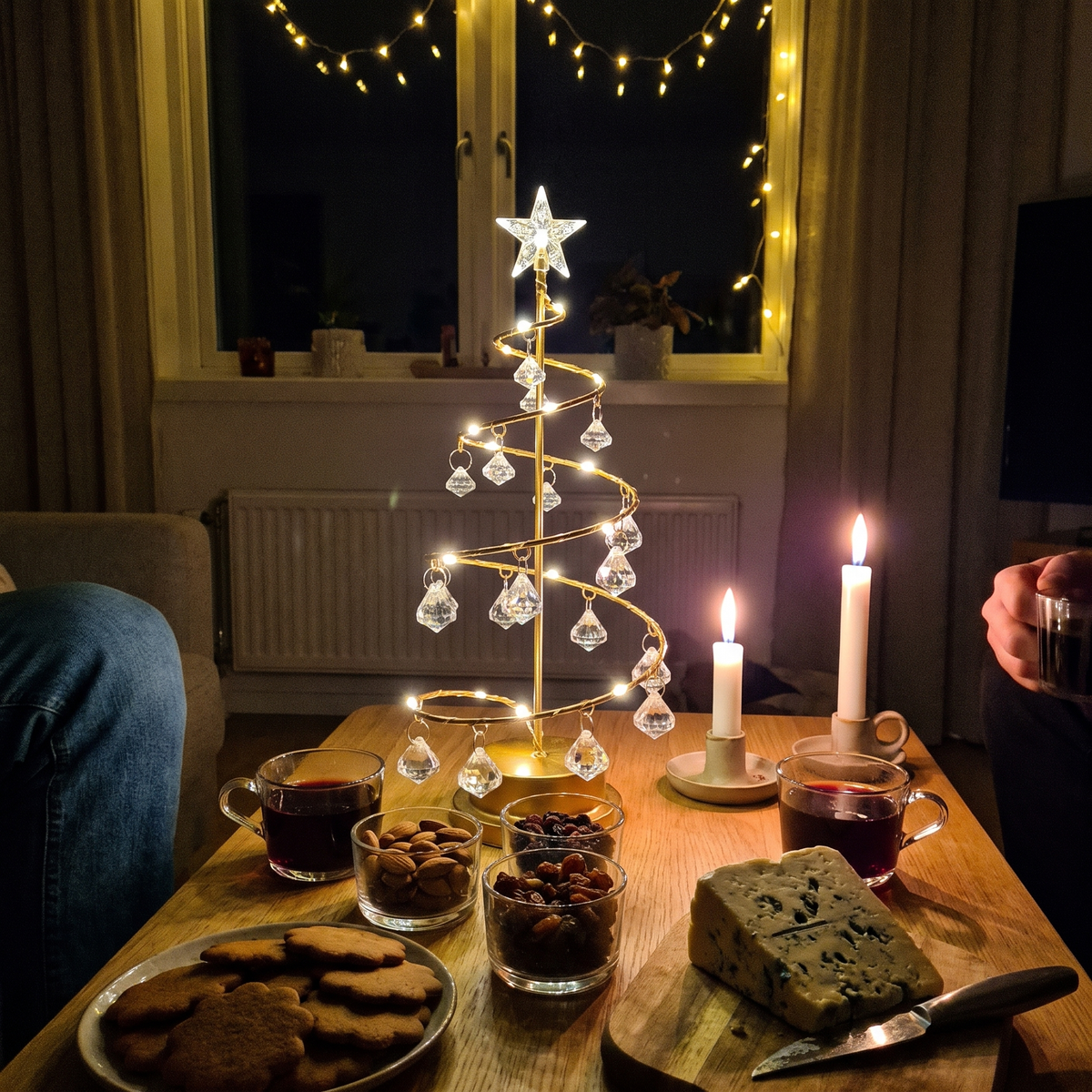 Tindra tänd mitt på soffbordet under en glöggkväll med pepparkakor, ädelost och levande ljus